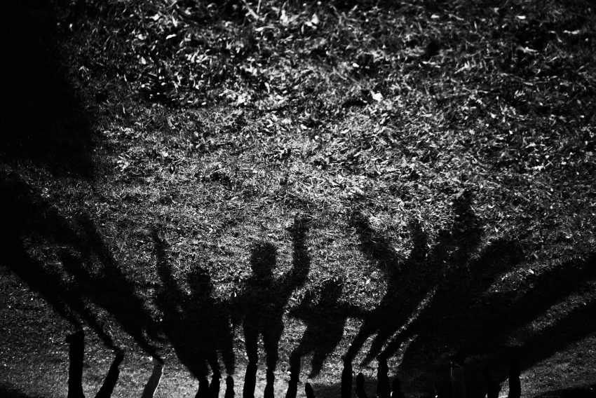 A dark silhouette of people joyfully jumping together on the grass