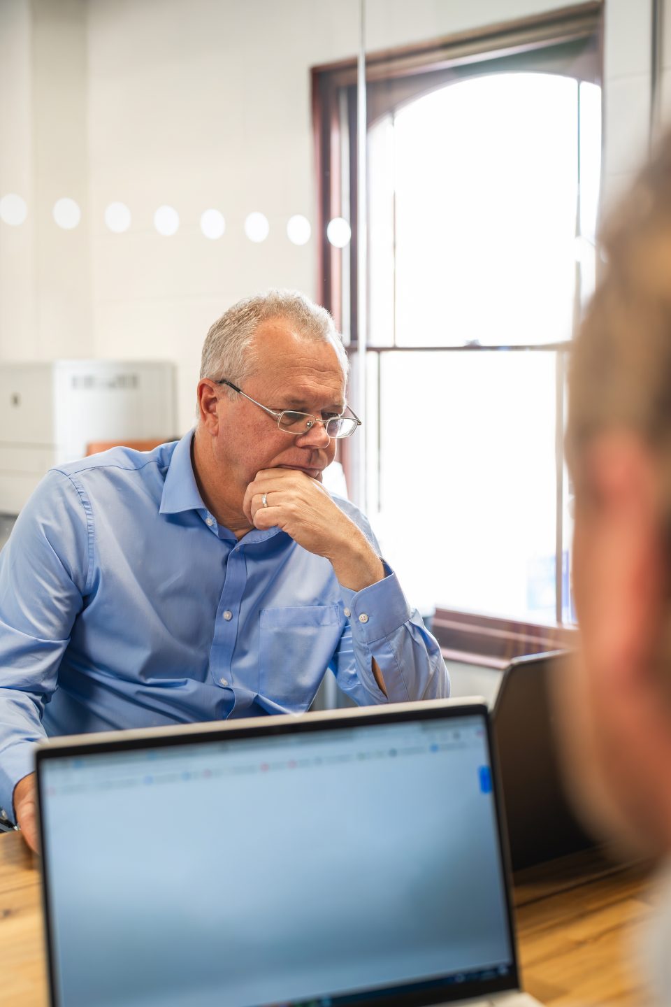 Two people in a meeting room, on their laptops across a wooden table
