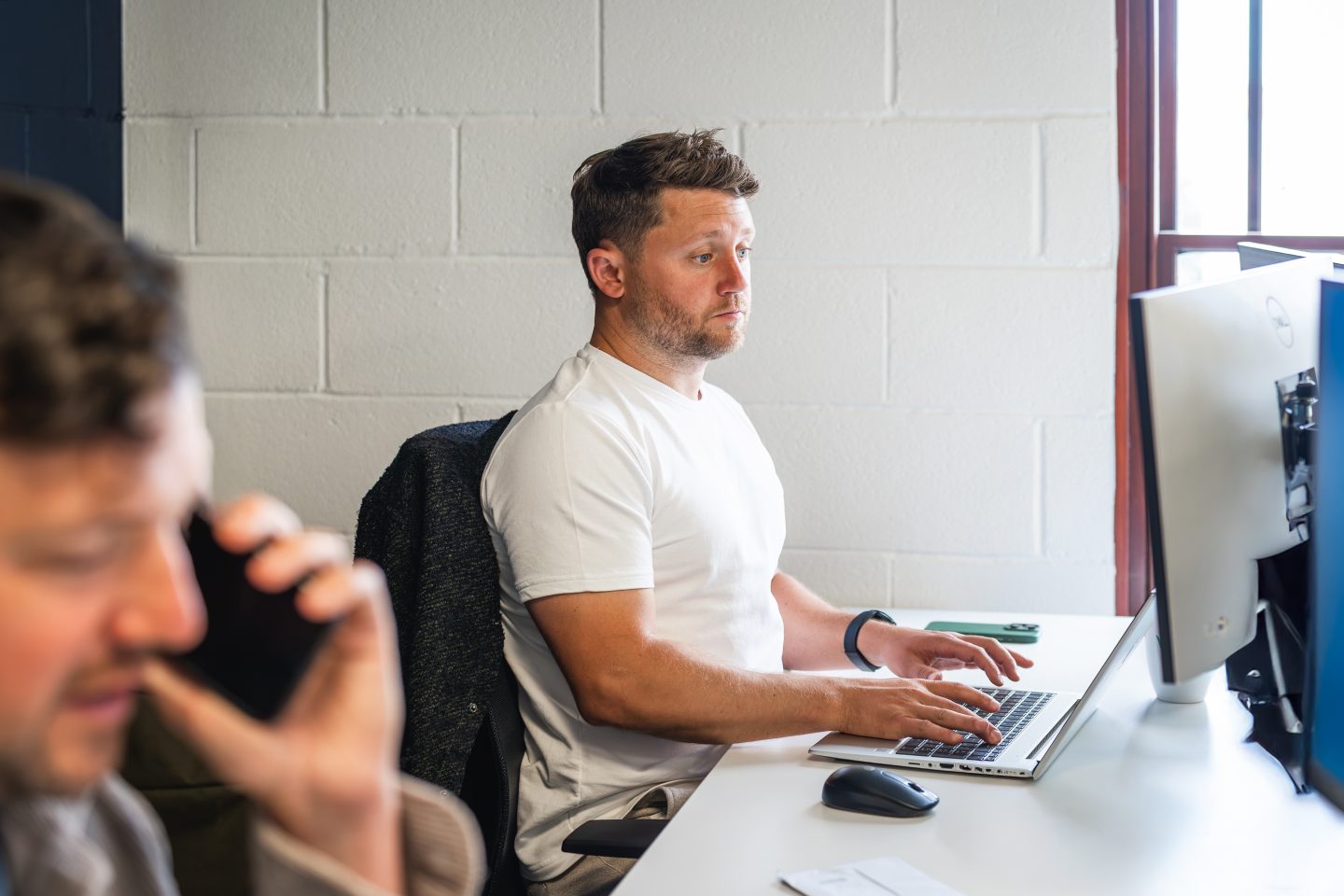 Two people are working at their desks; one is on a computer, while the other is having a phone call