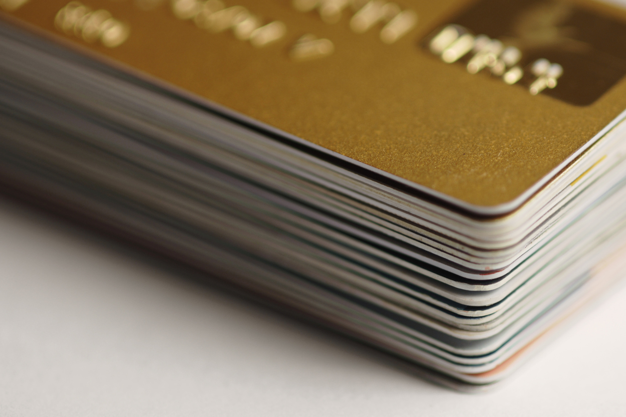 A corner of a pile of credit cards with a gold credit card on top.