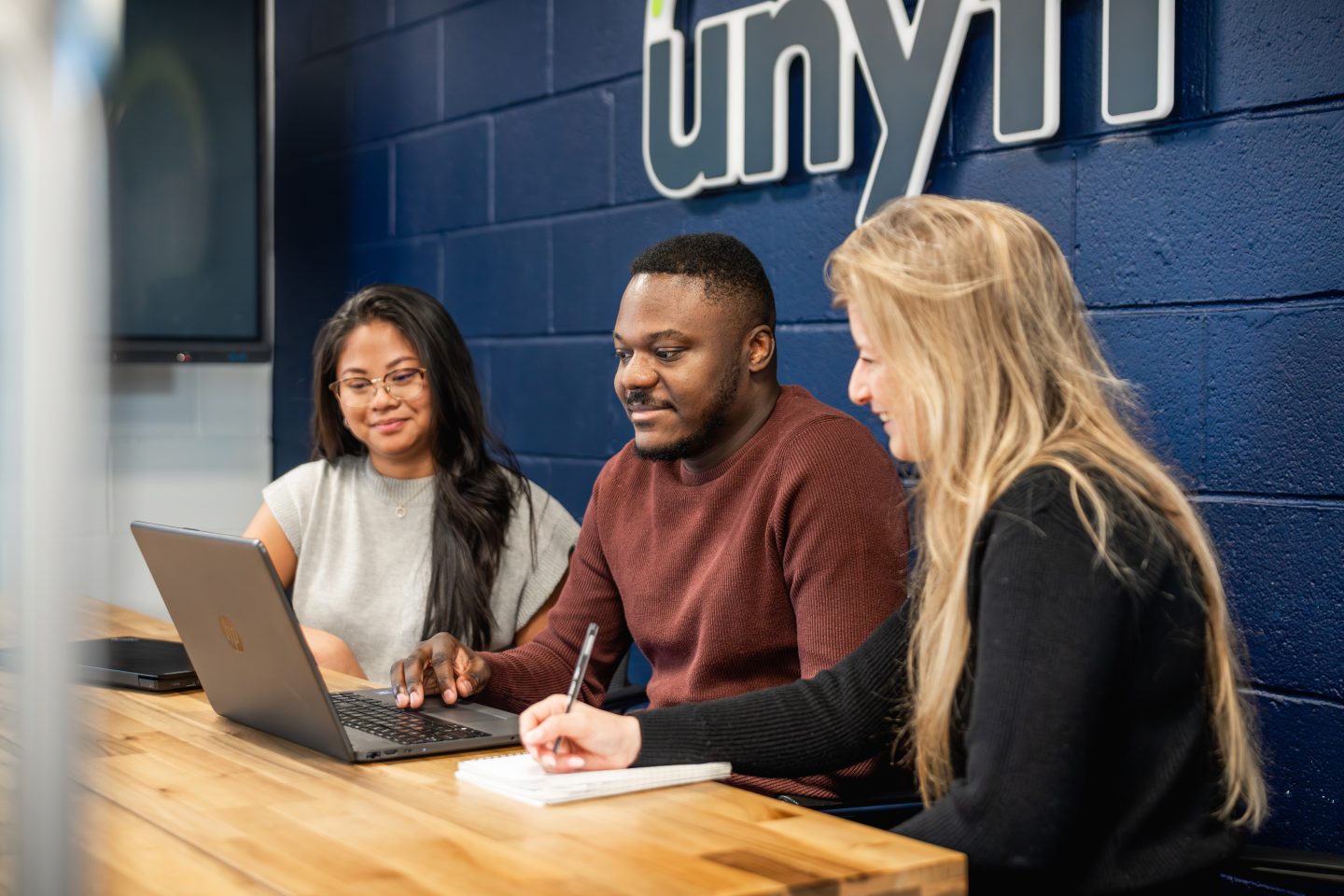 three people working together in a meeting room and looking at a laptop screen
